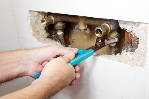 Plumber's hands have a two fisted grip on a wrench as he loosens a nut to fix a leak in a shower